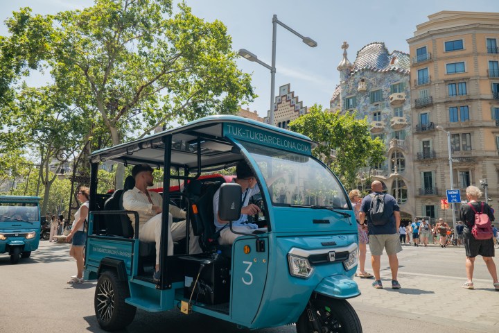 Blue tuk-tuk vehicle on a bustling street with people and colorful buildings in the background.
