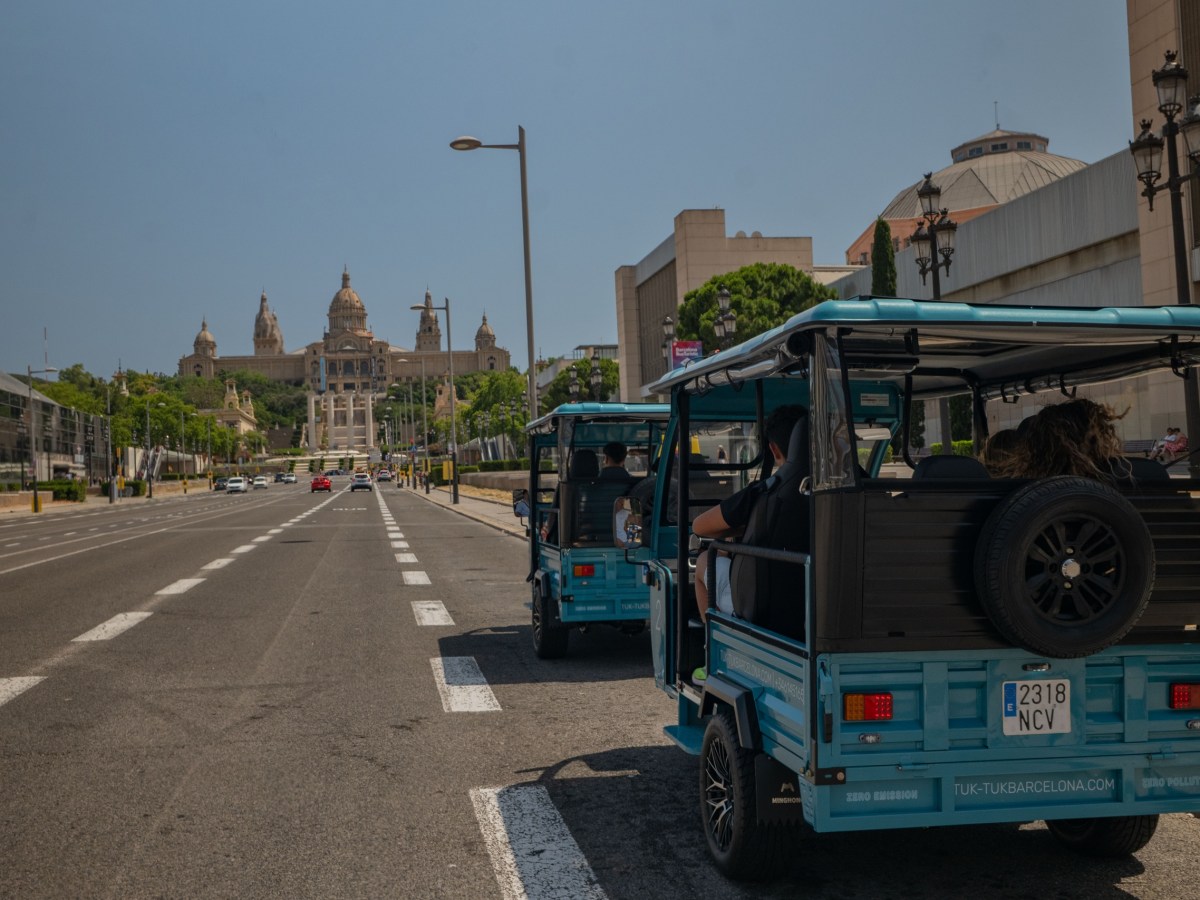 Street view of blue electric tuk-tuks driving towards a grand building in Barcelona.