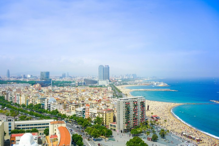 Aerial view of a city with tall buildings, beach, and blue ocean under a clear sky.